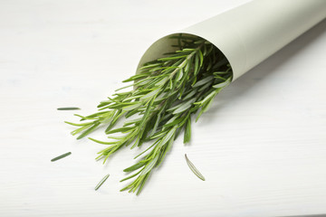 Rosemary fresh herb on paper cone. White wooden background.