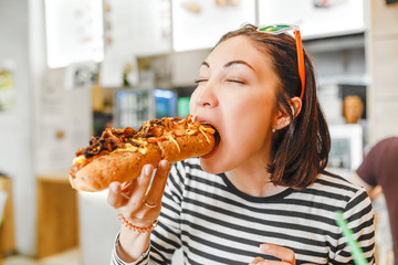 Young pretty girl eating big hotdog in fastfood restaurant