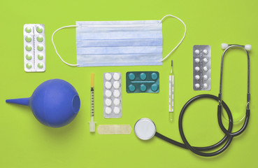 Medical equipment on green background. Enema, blisters pills, notepad, stethoscope, syringe,...