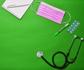 Workplace of a modern doctor. Laptop, wireless mouse, stethoscope, pills, syringe on green pastel...