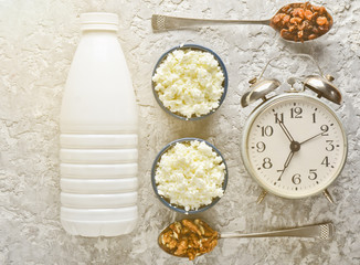 Healthy, dietary food. Morning breakfast. A bottle of yogurt, bowls with cottage cheese, spoons with walnuts and raisins, alarm clock on a gray concrete table. Top view. Flat lay food..