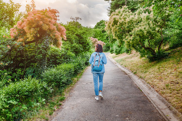 Hipster girl walks along the path in the city park and looking at the blooming trees at spring time