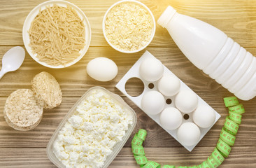 Diet, healthy food. Bottle of yogurt, crispy round bread, buckwheat noodles, oatmeal, cottage cheese, egg tray on a wooden table. Ruler for waist measurement. The concept of losing weight.