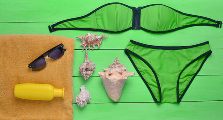 Swimsuit, towel, sunscreen, seashells, sunglasses on green wooden boards. The concept of a resort rest on the beach, top view.