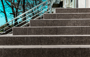 Stone granite stairs steps background with metallic aluminium handle. Red brown modern stairs. Entrance to the shop in the city street on blue sky and trees background.