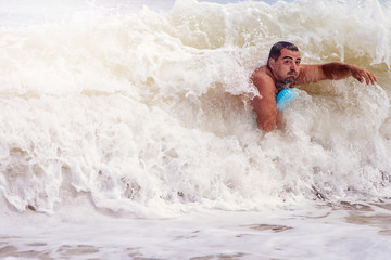 A man swims in the raging sea, it covers a huge wave.