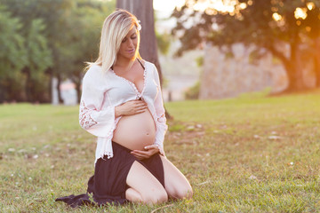 Blonde pregnant woman in a park, with pleasure expecting baby. Outdoors, on a sunny day. Second...