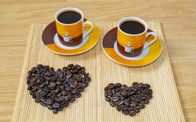 Two cups of coffee and a heart made of coffee beans.