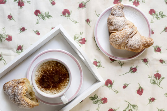 cornetti con cappuccino o caffe latte e colazione in vassoio bianco e tazza e piatti bianchi bordati di rosa con tovaglia  con rose rosse
