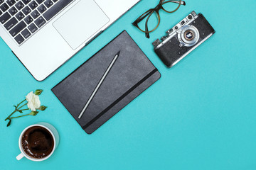 office desk with a laptop a cup of coffee, glasses, a notebook and accessories on a bright blue background with space for text. Top view with copy space, flat lay