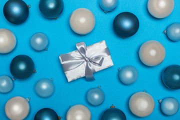 Obraz na płótnie Canvas a view from above on New Year's and Christmas decorations, toys and a gift in a festive holiday paper with a bow. Gift and Christmas balls on a bright blue background. flat lay
