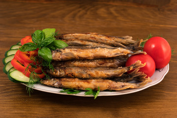 Fish dish of fried small capelin with garnish of vegetables and herbs.