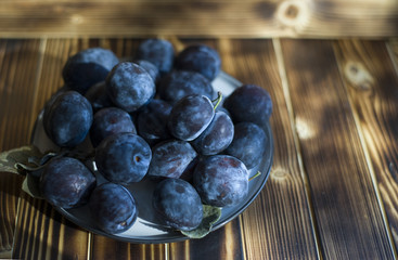 on a dark wooden background is a plate of plums