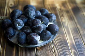 on a dark wooden background there is a plate with plums (background with hard light and condensate on plums)