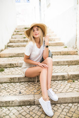 Fototapeta na wymiar Happy young woman in summer hat sitting on the stairs in city street