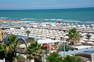 Riccione, Italy, June 18, 2018. Beach umbrellas, tourists, gazebos and sun beds at Italian sandy beaches. Adriatic coast. Summer season - obrazy, fototapety, plakaty