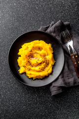 Mashed potato with pumpkin in black bowl. Dark background. top view