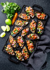 PERUVIAN FOOD. Choros a la chalaca. Big mussels, choros zapatos seasoned with purple onion, tomatoes, corn and lemon. Top view, black background. Traditional peruvian dish