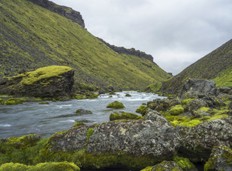 View on blue water stream and green moss covered stones and hills in Eldgja gorge in Iceland...