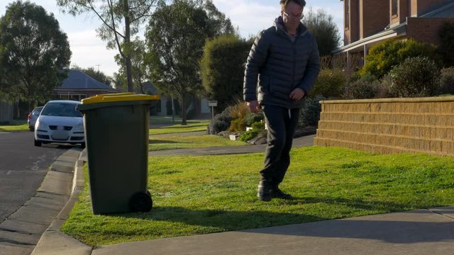 Man putting out yellow recycling wheelie bin to the curb side