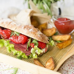 sandwich with ham, cream cheese, lettuce leaves, arugula, red pepper, baked potatoes, ketchup on a white wooden background with a floral fabric