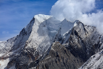 Chenadorje, holy snow mountain in Daocheng Yading Nature Reserve - Garze, Kham Tibetan Pilgrimage region of Sichuan Province China. Clouds blowing off the top of the snow capped mountain with blue sky