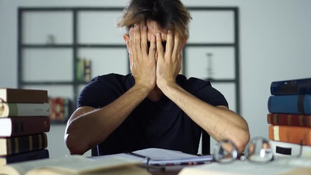 A tired nerd falling asleep on a bunch of books
