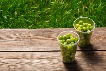 fresh gooseberry in plastic containers on a wooden table on a background of green grass