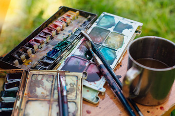 Palette of watercolor paints and brushes on the wooden background.
