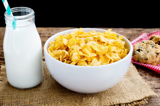 Cornflake cereals on white bowl with milk glass on table.