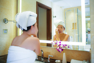 Obraz na płótnie Canvas lifestyle fresh portrait of young happy and beautiful Asian Chinese woman at home or hotel bathroom wrapped in toilet towel applying makeup cheerful and natural in female beauty and skin care .
