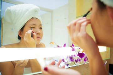 Obraz na płótnie Canvas lifestyle fresh portrait of young happy and beautiful Asian Chinese woman at home or hotel bathroom wrapped in toilet towel applying makeup cheerful and natural in female beauty and skin care .