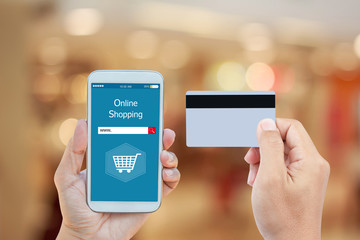 Hand holding smart phone with online shopping on screen and credit card over blurred in shopping mall background for mobile banking payment online concept