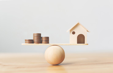 Wooden home and money coins stack on wood scale. Property investment and house mortgage financial real estate concept