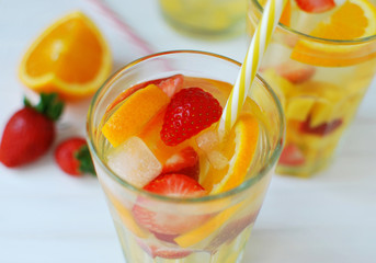 Refreshing summer drinks with strawberries and orange slices. Iced fruit drink in glass. Closeup view on white wooden background.