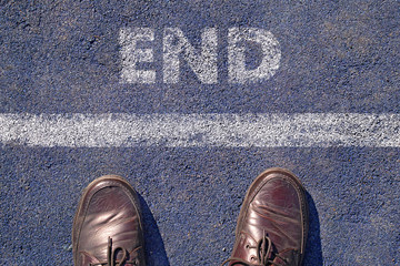 man feet in brown leather shoes standing before shabby sign end written on asphalt, top view