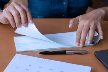 Business woman hand pullingout a check from cheque book after signing and writing, working at office with calendar and pen on the wooden table.