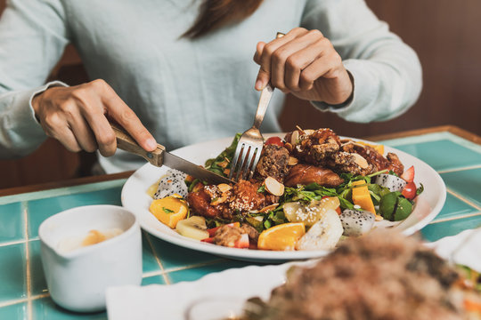 Young Woman Using Knife And Fork To Cutting Meat In Restaurant