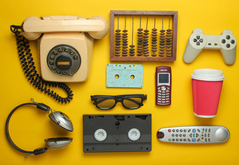 Retro objects on a yellow background. Rotary telephone, audio cassette, video cassette, gamepad, 3d glasses, tv remote, headphones, push-button phone. Analog media technology of the past. Flat lay.. - obrazy, fototapety, plakaty