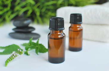peppermint essential oil in brown bottles, spa stones and white towels.