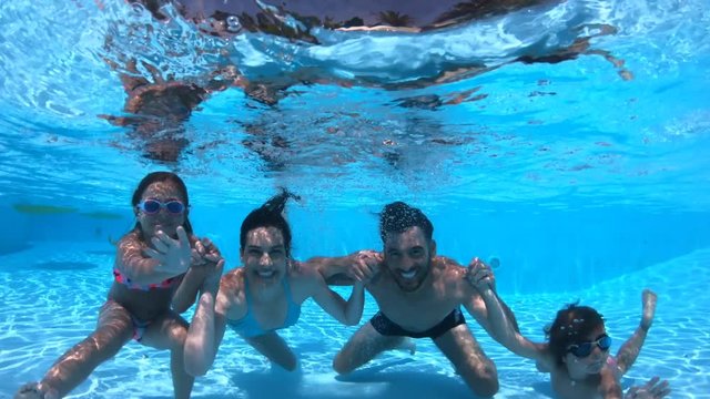 Family at the pool waving at camera underwater