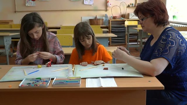 A teacher and four children. the teacher teaches students to model plasticine