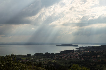 Naklejka na ściany i meble Sun rays coming out through the clouds over an island on a lake