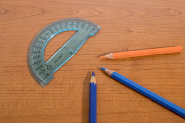 Stationery products, a protractor and some colored pencils on a wood table