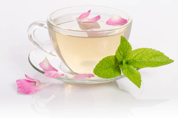 Glass cup of Tea with mint leaves and rose petals on light table