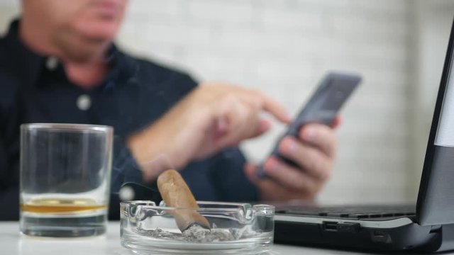 Blurred Image with Businessman Using Mobile Text and Smoking a Cigar