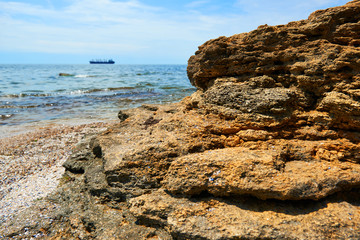 beautiful sea landscape with cargo ship on horizon, closeup of stone on the beach, sea coast with high hills, wild nature