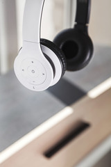 Closeup of minimalist white wireless plastic headset hanging in the air above a wooden shelf blurred in background in bright sunlight
