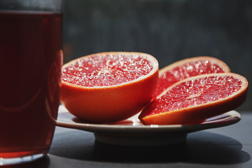 Fresh red grapefruit cut in pieces sparkling with juice in sunlight with transparent glass filled with red colored drink