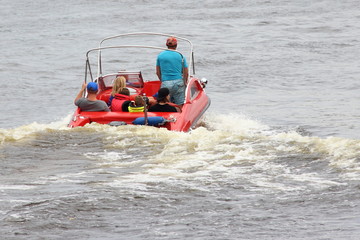 Travel, water activities - red 18-ft motor boat with passengers slowly floating away on the water, rear view